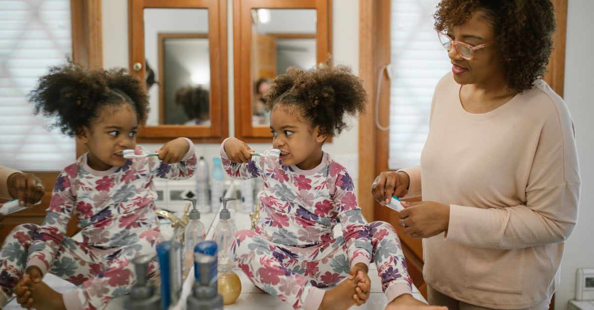 A mother helps her daughter in pajamas brush her teeth during a morning routine in the bathroom.